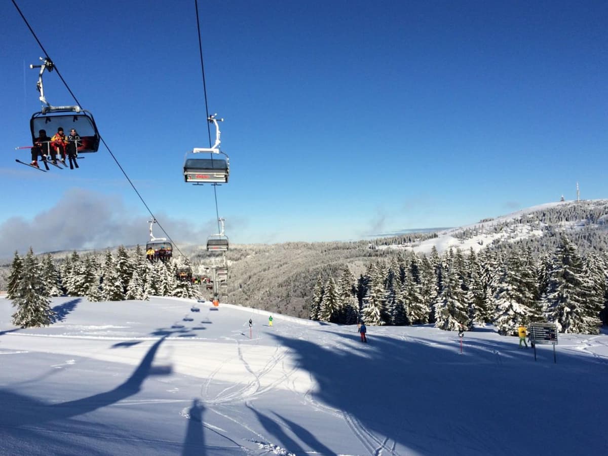 Skilift im Winter mit viel Schnee vor blauem Himmel und einigen Skifahrern